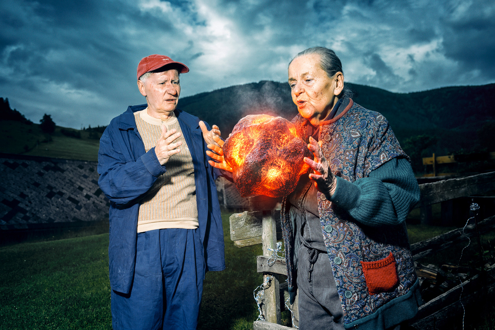 Älterer Mann und Frau im Freien, die auf einen leuchtenden, lavaartigen Meteoriten zwischen ihnen zeigen.